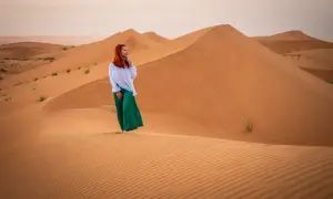 Kobieta w zielonej spódnicy i białej koszuli stoi na wydmach. Czy Oman jest bezpieczny? Tak, to piękny kraj do zwiedzania.