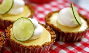 Små key lime pies med vispad grädde och limeklyfta på en rödvitrutig duk.