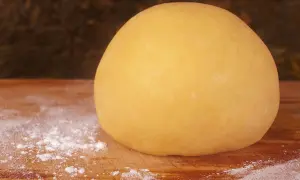 Impasto di pasta frolla per pastiera, 1 kg, pronto per essere steso su un tagliere infarinato.