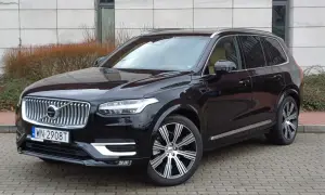 Elegancki, czarny Volvo XC90 z chromowanymi felgami stoi na brukowanym podjeździe.