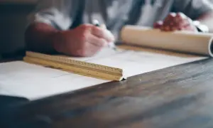 Architekt rysuje na planach, obok leży linijka i zwój papieru.