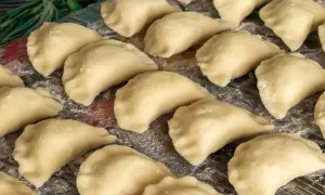 Gotowe do gotowania ciasto na pierogi, ułożone na desce, posypane mąką.