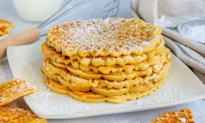 Stapel goldbrauner Waffeln ohne Backpulver, bestäubt mit Puderzucker. Daneben liegen weitere Waffeln.