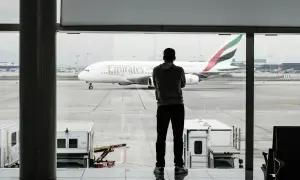 Mężczyzna w bluzie patrzy na samolot Emirates. Czeka na swój bagaż podręczny.