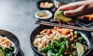 En hand pressar lime över en skål med nudlar och grönsaker, perfekt vin till asiatisk mat.