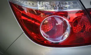 Gros plan sur un feu arrière de voiture rouge. Le feu de position arrière ne fonctionne plus, reflétant le ciel et les arbres.