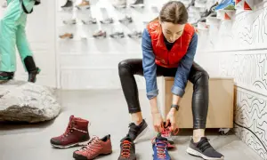 Kobieta przymierza buty trekkingowe, zastanawiając się, czy buty trekkingowe powinny być większe. Na podłodze kilka par butów.