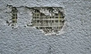 Uszkodzona szara elewacja z siatką zbrojeniową widoczną pod tynkiem. Czas na naprawę elewacji!