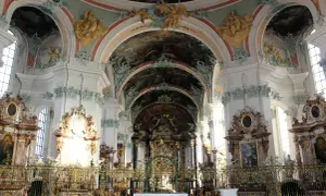 Wnętrze kościoła w stylu barokowym, z bogatymi zdobieniami, freskami na sklepieniach i złotymi elementami.