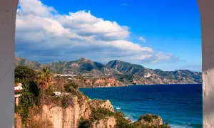 Vue panoramique de la côte andalouse, parfaite pour un guide Malaga. Falaises rocheuses, mer bleue et montagnes verdoyantes sous un ciel d'azur.