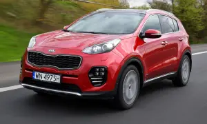 Czerwony Kia Sportage IV pędzi po drodze, otoczony zielenią.