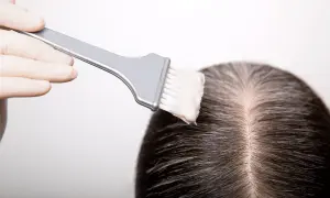 Guanto e pennello applicano tinta sui capelli scuri, mostrando come fare la tinta in casa per un cambio look.