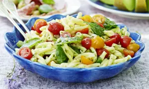 En härlig pastasallad vegetarisk med körsbärstomater, basilika och pinjenötter i en blå skål.