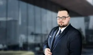Mężczyzna w garniturze i okularach na tle nowoczesnego budynku.
