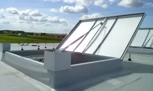 Otwarta klapa dymowa na dachu, z widokiem na zielone pola i błękitne niebo z chmurami.