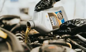 Händer med handskar häller olja i en bilmotor. En flaska med "MAXI PERFORMANCE" olja. Vilken olja till min bil?