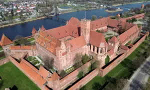 Malbork, największy zamek w Europie, rozciąga się wzdłuż rzeki. Potężne ceglane mury i czerwone dachy tworzą imponujący widok.
