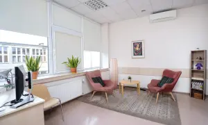 Jasne, przytulne wnętrze gabinetu psychologicznego z dwoma różowymi fotelami i stolikiem.
