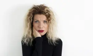 Kobieta z kręconymi blond włosami i zmartwioną miną, opierająca policzek na dłoni. Wyraz twarzy sugeruje depresję reaktywną.