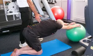 Un homme fait des exercices pour soulager son arthrose lombaire, guidé par un kinésithérapeute.