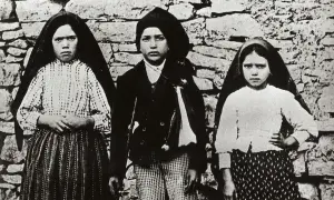 Trójka dzieci, w tym siostra Łucja z Fatimy, pozuje przed kamiennym murem.