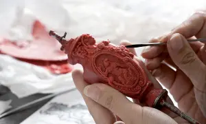 Mani esperte rifiniscono un oggetto in cera rossa, un'opera d'arte che ricorda la **fondazione Cologni**. Dettagli intricati prendono forma sotto gli strumenti.