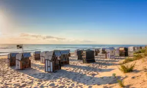 Reihe von Strandkörben am Strand Deutschland, mit Blick auf das Meer und den blauen Himmel.