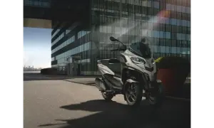 Nowoczesny Piaggio MP3, czy wersja 400 czy 500, parkuje przed szklanym budynkiem.