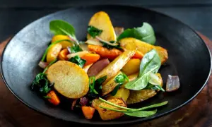 En tallrik med ugnsrostade rotfrukter, inklusive potatis, morötter och rödlök, blandat med färsk spenat. En härlig rotfrukter lista för en god måltid.