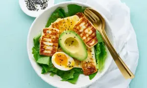 Idealne keto śniadanie: grillowany ser halloumi, awokado, jajko na miękko i świeża sałata, posypane czarnym sezamem.