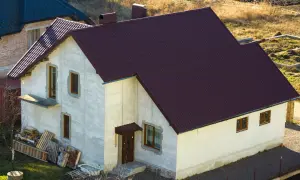 Nowy dom w zabudowie siedliskowej, z ciemnobordowym dachem i jasnymi ścianami, czeka na wykończenie.