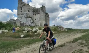 Młody mężczyzna na rowerze przemierza malowniczą trasę po Jurze Krakowsko-Częstochowskiej, mijając ruiny zamku.