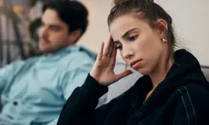 Zmartwiona kobieta z ręką na czole, podczas gdy jej mąż wmawia jej chorobę psychiczną.