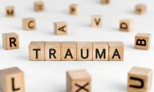Drewniane klocki układają się w słowo TRAUMA, otoczone innymi literami. To obraz symbolizujący trudne doświadczenia.