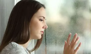 Smutna dziewczyna patrzy przez zaparowane okno. Jej dłoń dotyka szyby, jakby szukając wyjścia z tej potocznie zwanej depresji psychicznej.