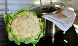 Świeży kalafior na kuchence, gotowy do ugotowania. Obok garnek z pokrywką i ściereczka.