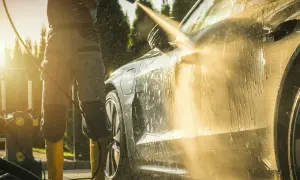 Słońce zachodzi, a Ty uczysz się, jak myć auto na myjni ciśnieniowej. Woda spływa po lśniącej karoserii.