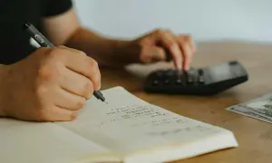 Ręce piszą w zeszycie i liczą na kalkulatorze. To może być planowanie budżetu, np. na dieta krajowa.