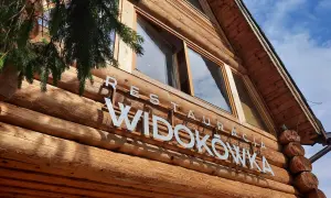 Drewniana restauracja Widokówka z białym napisem. Gałązka świerku zwisa z lewej strony.