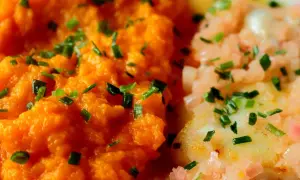 Purée de carotte onctueuse, parsemée de ciboulette fraîche, à côté d'un plat de poisson aux oignons roses. Un délice coloré.