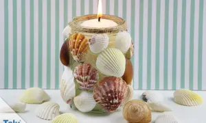 Kerzenglas mit Muscheln verziert, ein schönes Beispiel für basteln mit Muscheln. Ein warmes Licht scheint durch die maritime Dekoration.