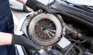 Mechanic holding a car clutch assembly with engine in background.