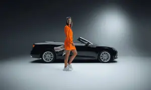 Frau in orangefarbenem Kleid neben schwarzem Cabrio. Ein toller Sixt Aktie Rabatt für Ihre nächste Fahrt!