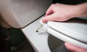 Montaż deski WC: ręka wsuwa trzpień mocujący do otworu w ceramice.