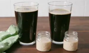 Zwei Gläser dunkles Bier und zwei kleine Gläser mit cremiger Flüssigkeit auf einem Holztisch.