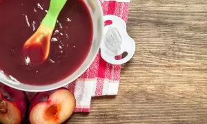 Schüssel mit pflaumenmus baby, Löffel, Schnuller und frische Pflaumen auf Holztisch.