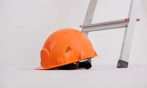 Pomarańczowy kask leży obok drabiny, gotowy do pracy.