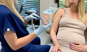Dentystka pokazuje ciężarnej pacjentce model szczęki, omawiając higienizację zębów w ciąży.