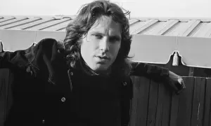 Jim Morrison, wokalista The Doors, oparty o drewniany płot, zamyślony.