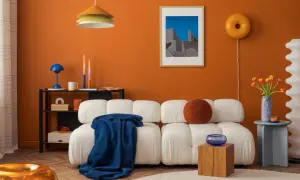 Nowoczesny salon z białą kanapą, pomarańczową ścianą i kolorowymi dodatkami.